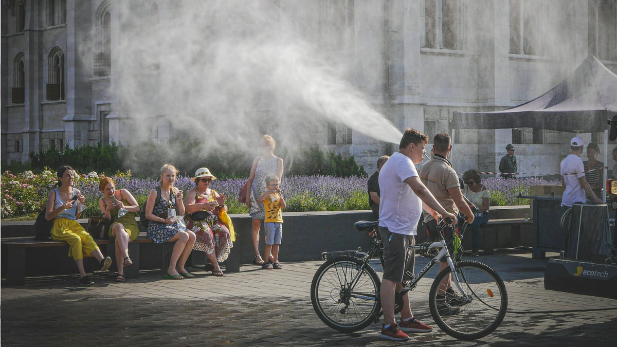 People sit outside amid water misters during a hot summer day.